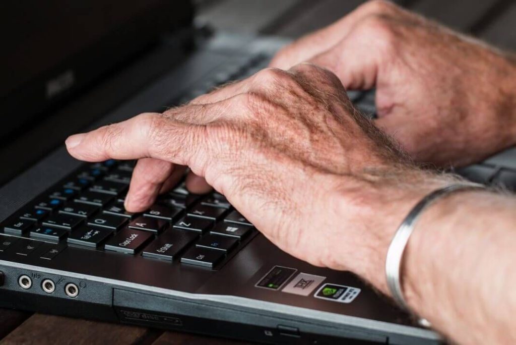 Imagen de las manos de un adulto mayor escribiendo sobre un teclado