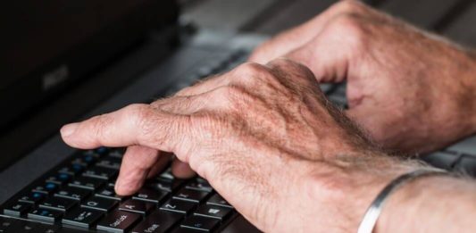 Imagen de las manos de un adulto mayor escribiendo sobre un teclado