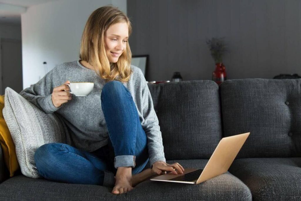 Joven mujer mira su ordenador con una taza de café en la mano